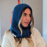 Woman wearing a blue knitted hood over her head, sitting indoors.
