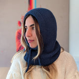 Woman wearing a navy blue knitted hood over her head, sitting indoors.