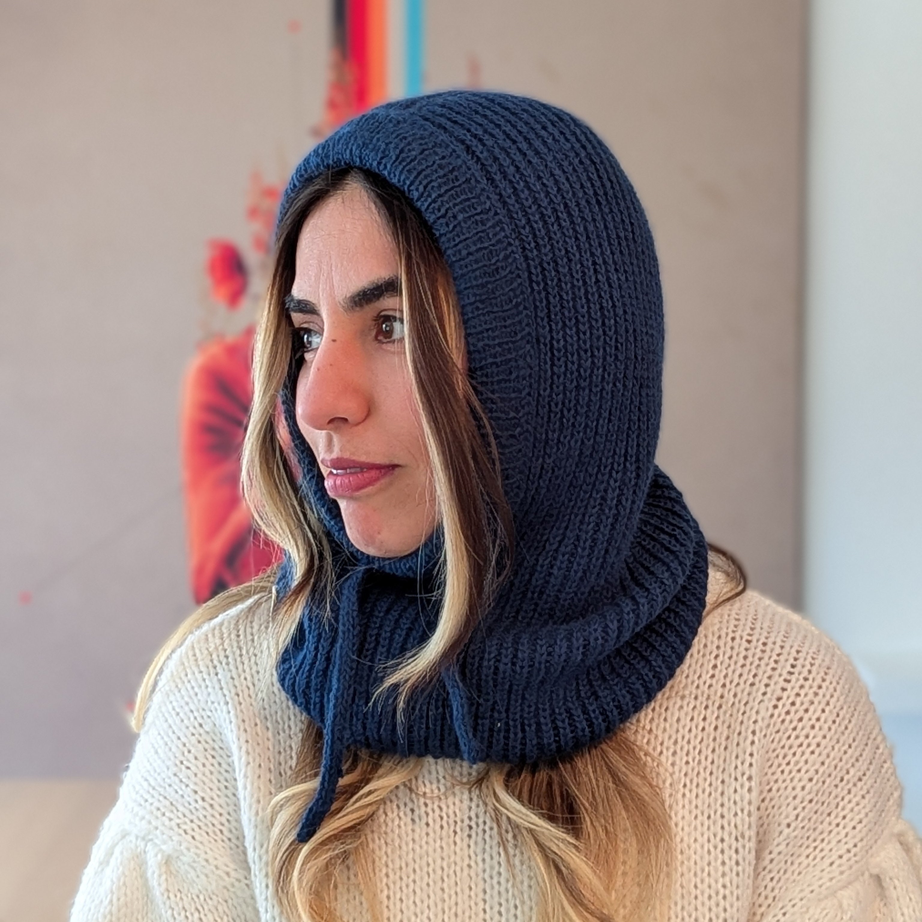 Woman wearing a navy blue knitted hood over her head, sitting indoors.