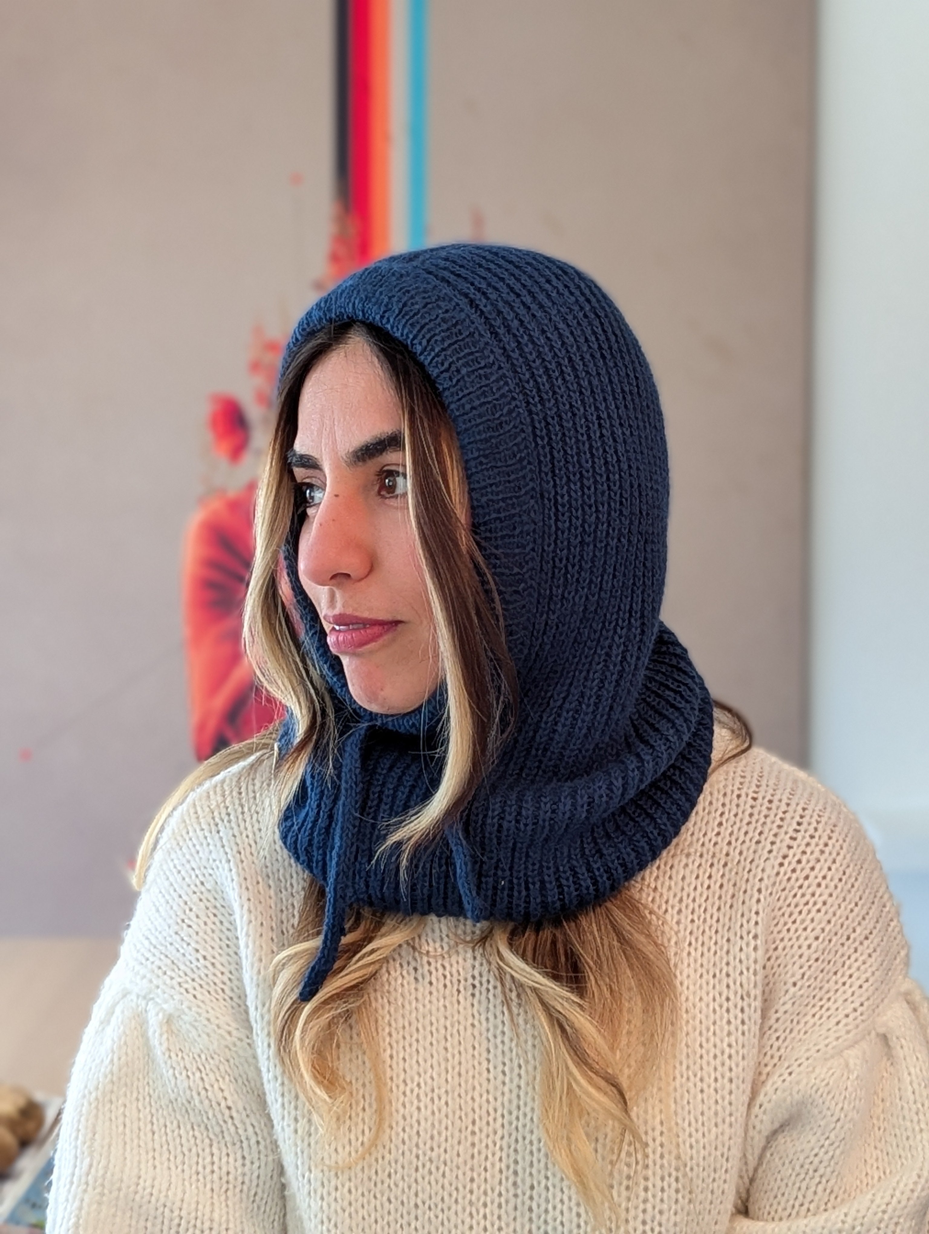 Woman wearing a navy blue knitted hood over her head, sitting indoors.