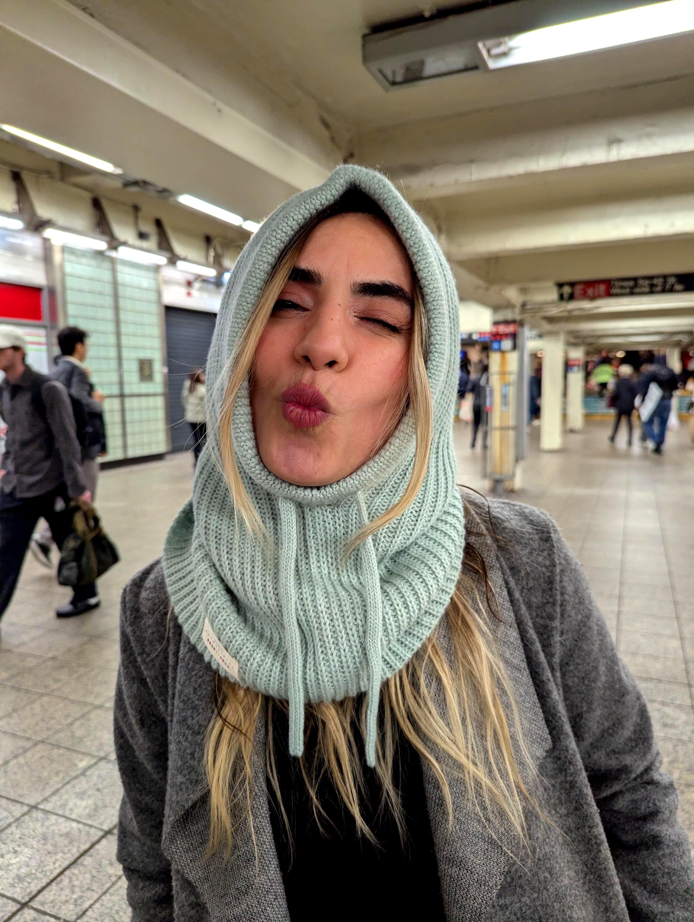 Person wearing a mint knitted hood and scarf in a subway station.