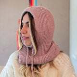 Woman wearing a pink knitted hood over her head with a neutral background