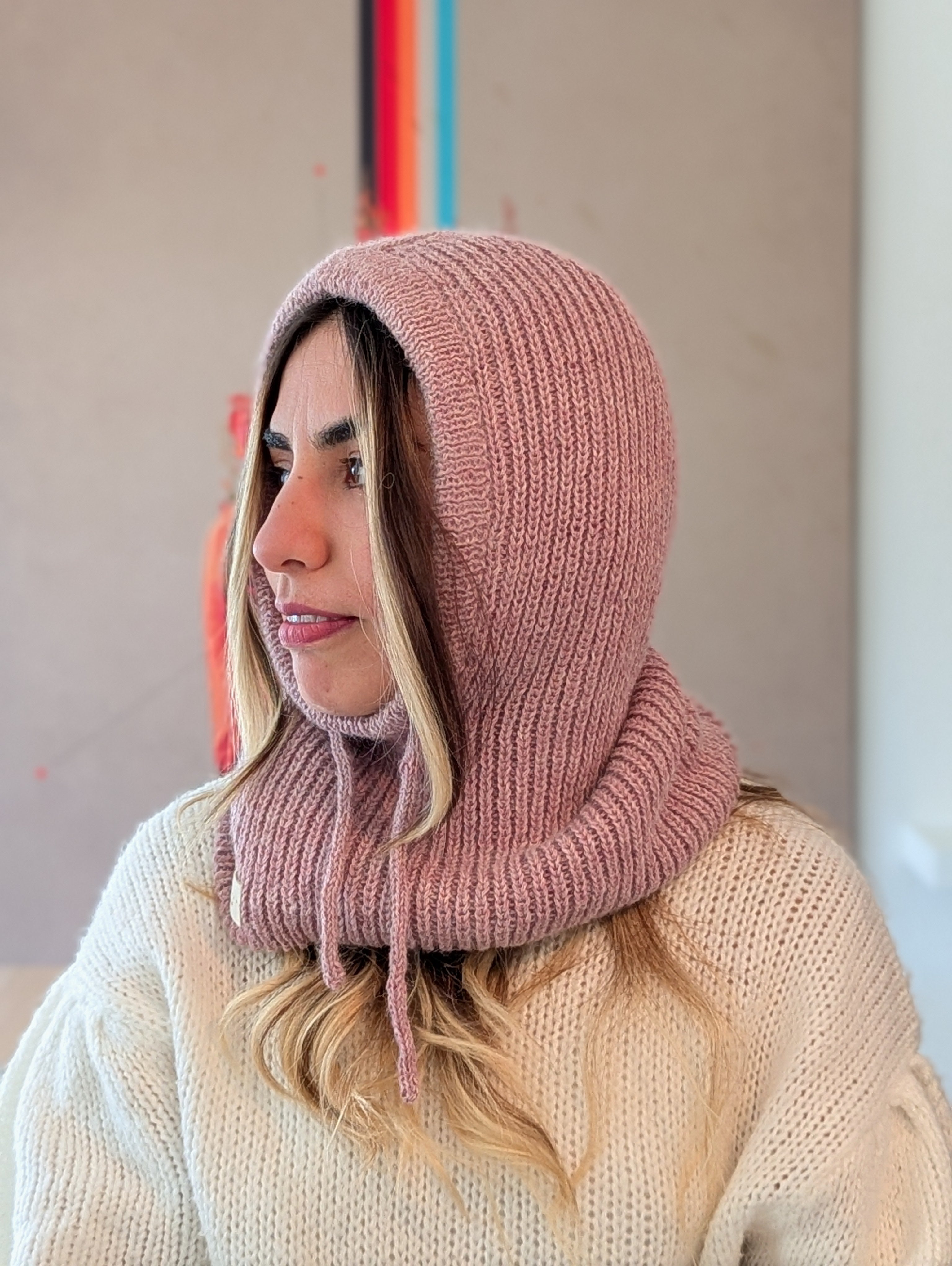 Woman wearing a pink knitted hood over her head with a neutral background