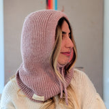 Person wearing a pink knitted hood over a white sweater with a neutral background