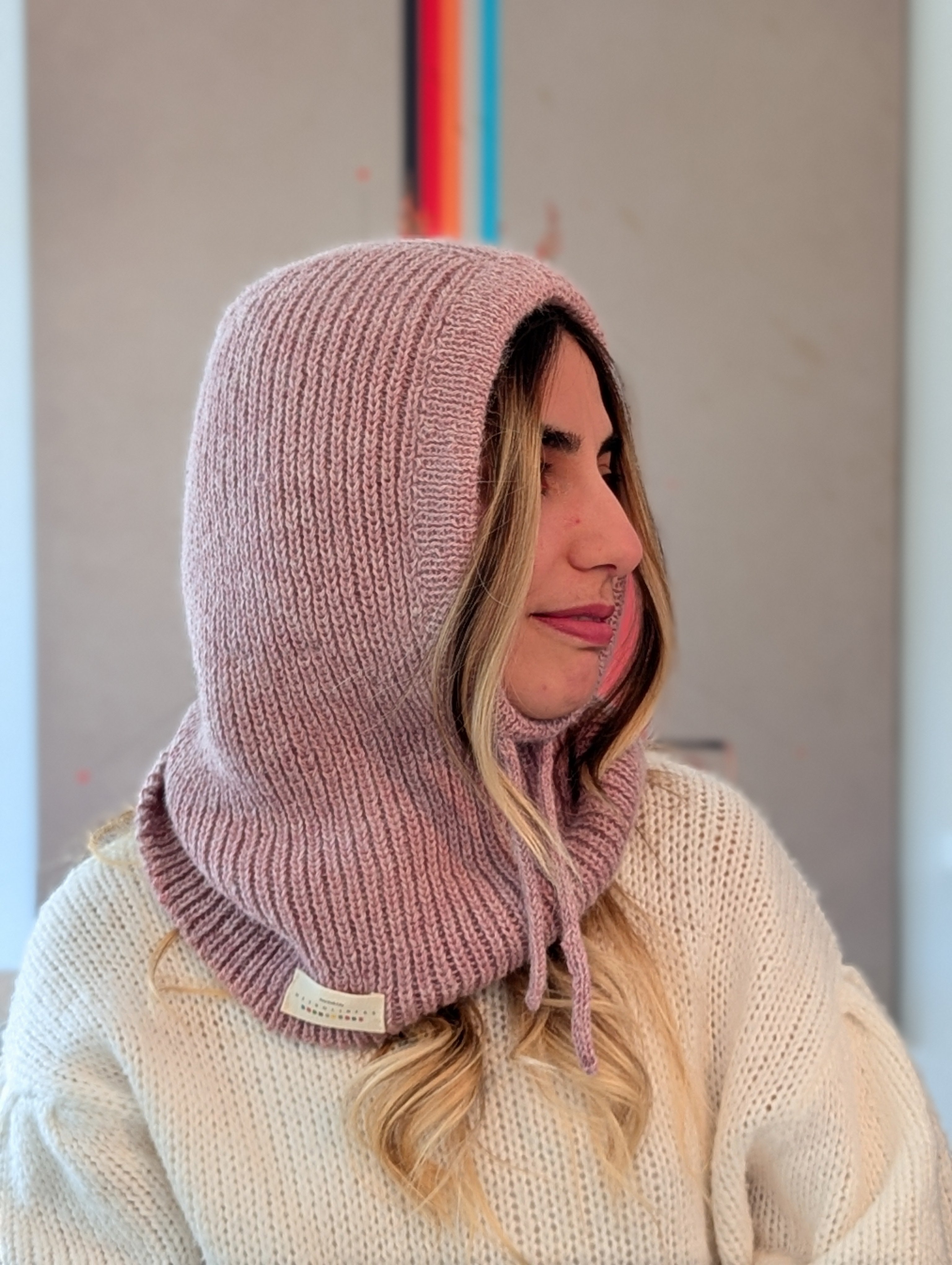Person wearing a pink knitted hood over a white sweater with a neutral background