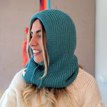 Woman wearing a teal knitted hood over her head with a beige sweater underneath.