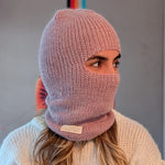 Person wearing a pink knitted balaclava with a neutral background