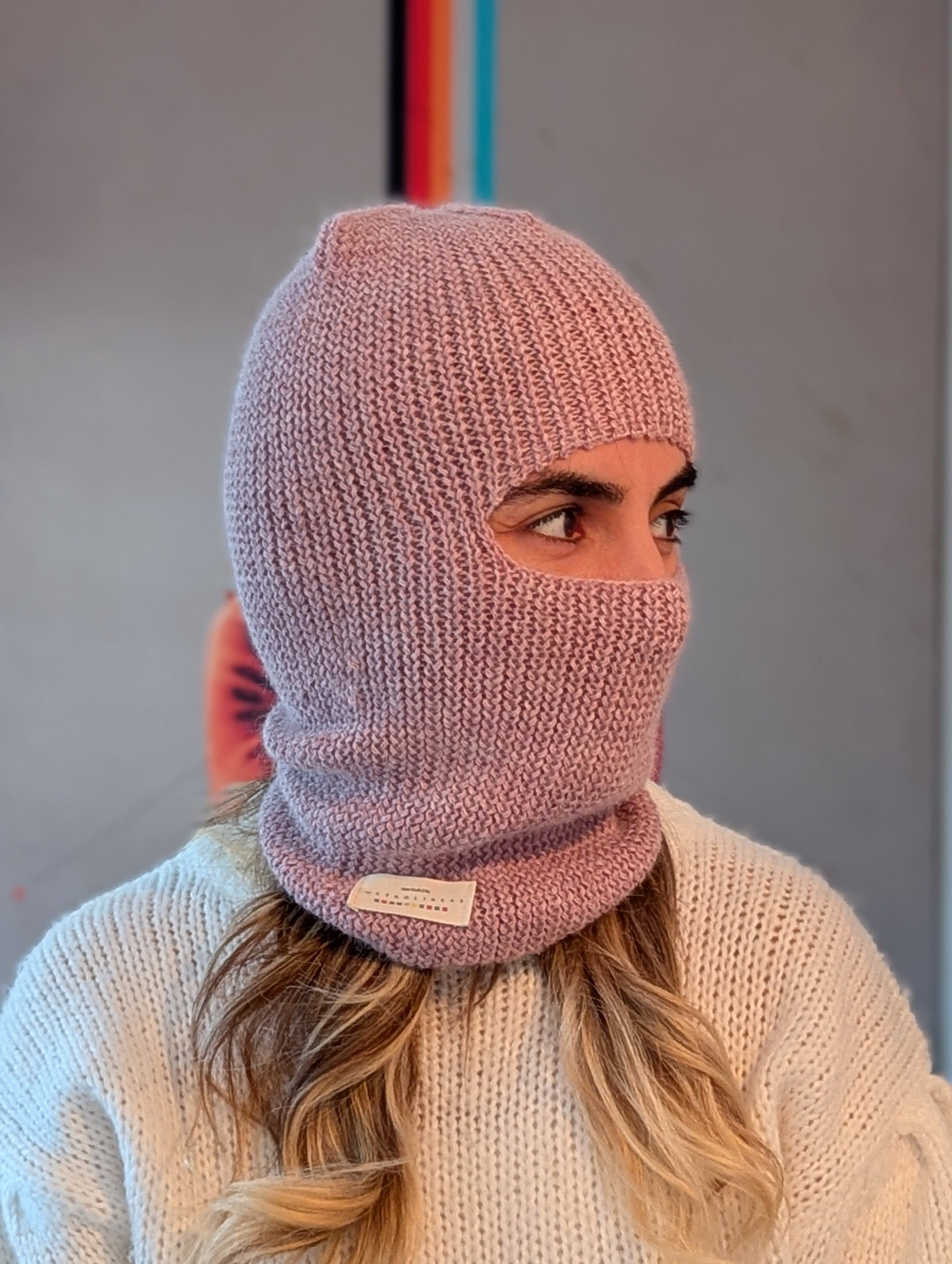 Person wearing a pink knitted balaclava with a neutral background