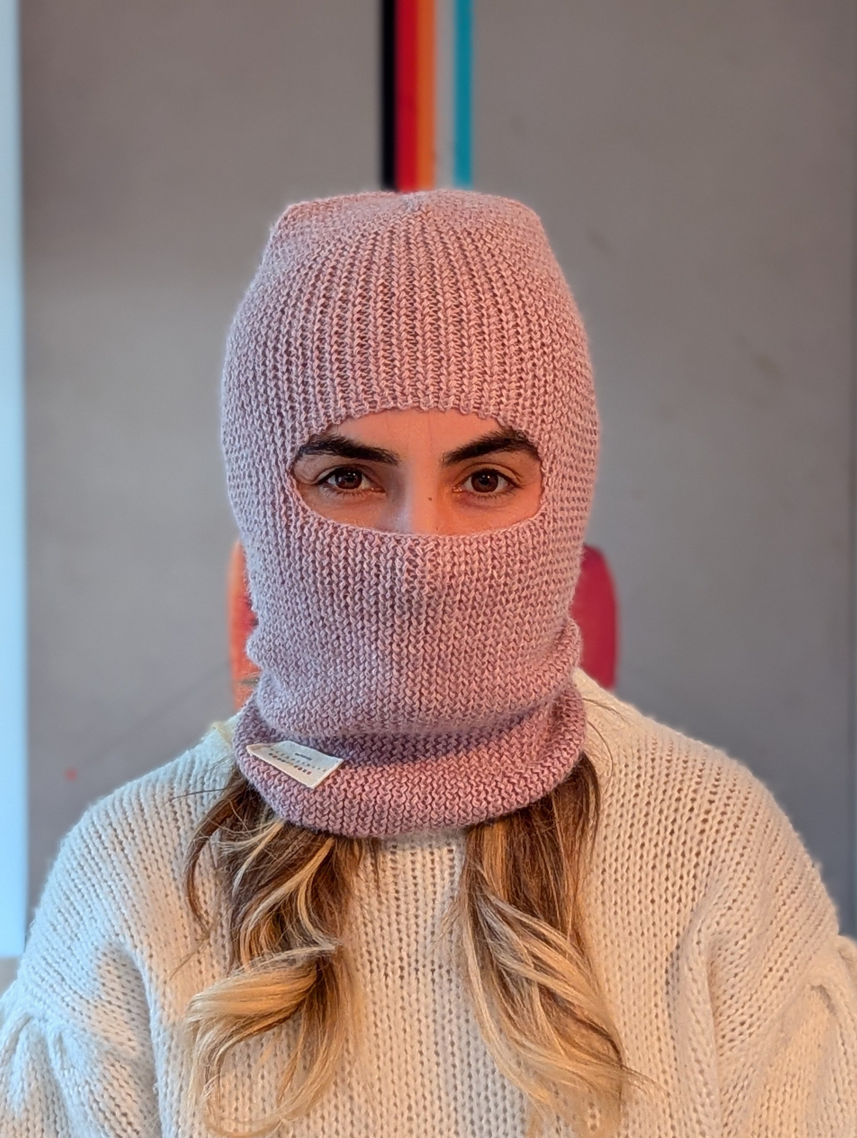 Person wearing a pink knitted balaclava with a blurred background
