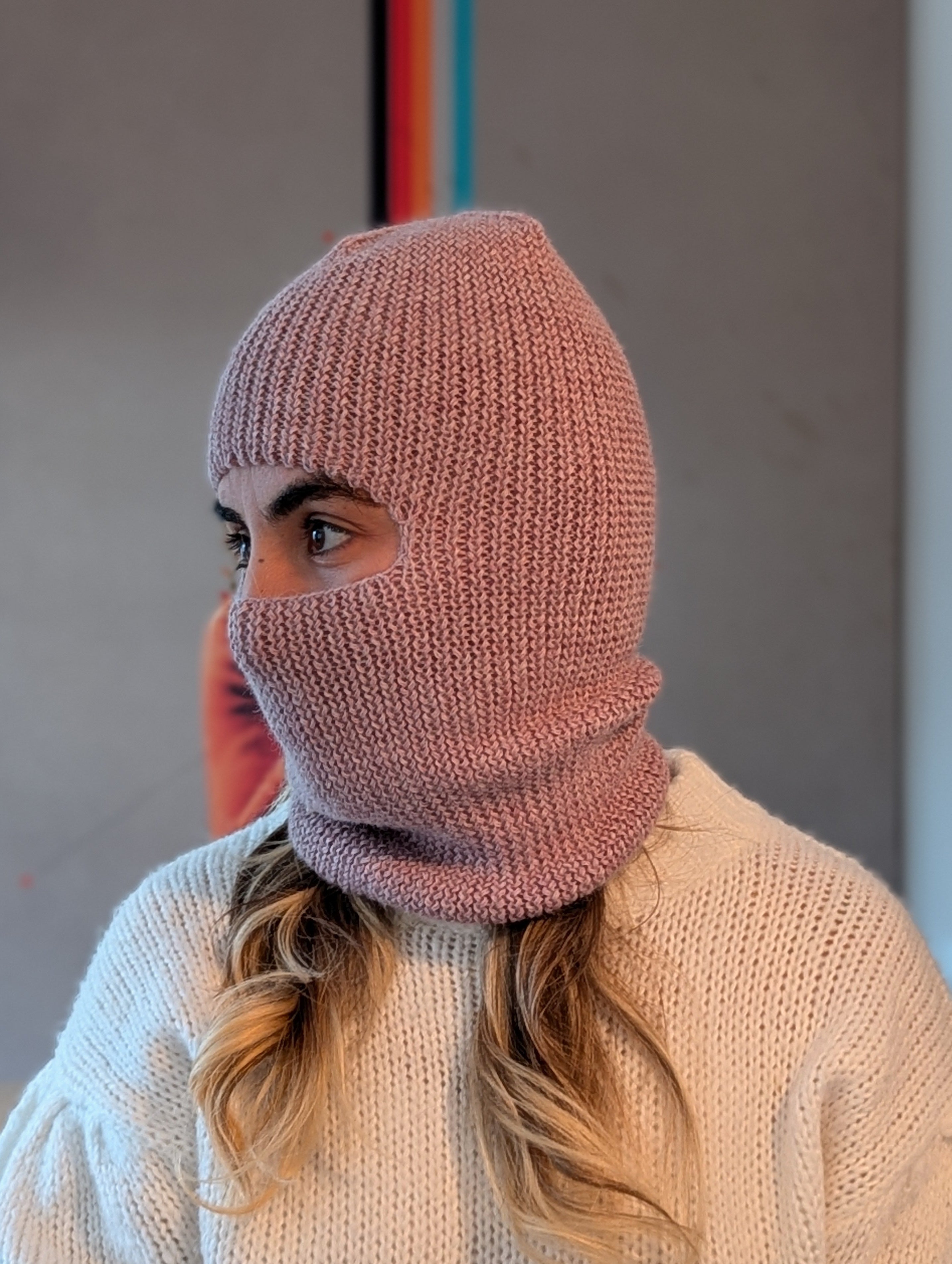 Person wearing a pink knitted balaclava in an indoor setting