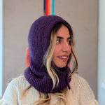 Woman wearing a purple knitted hood over a white sweater with a neutral background