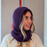 Woman wearing a purple knitted hood over a white sweater with a neutral background