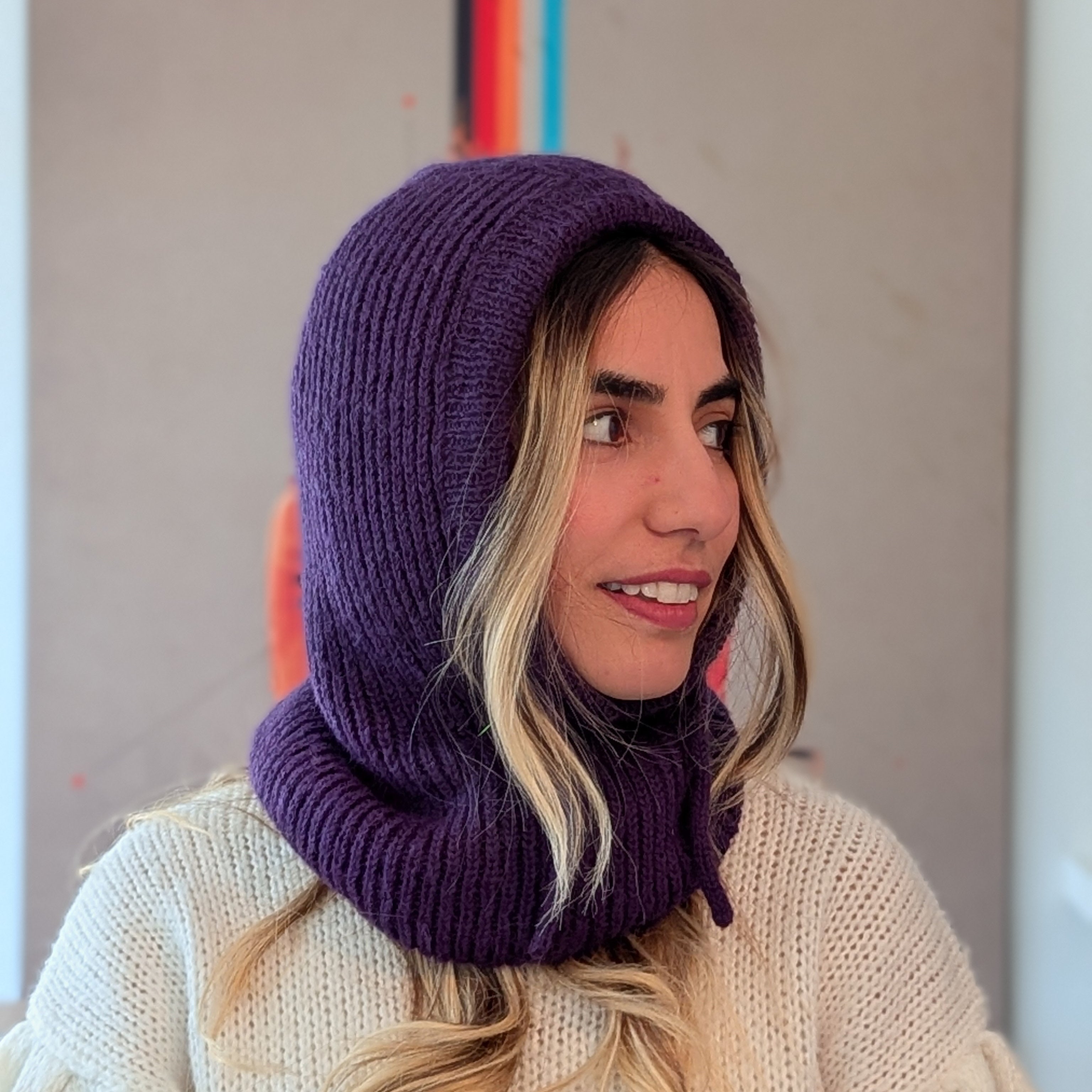 Woman wearing a purple knitted hood over a white sweater with a neutral background