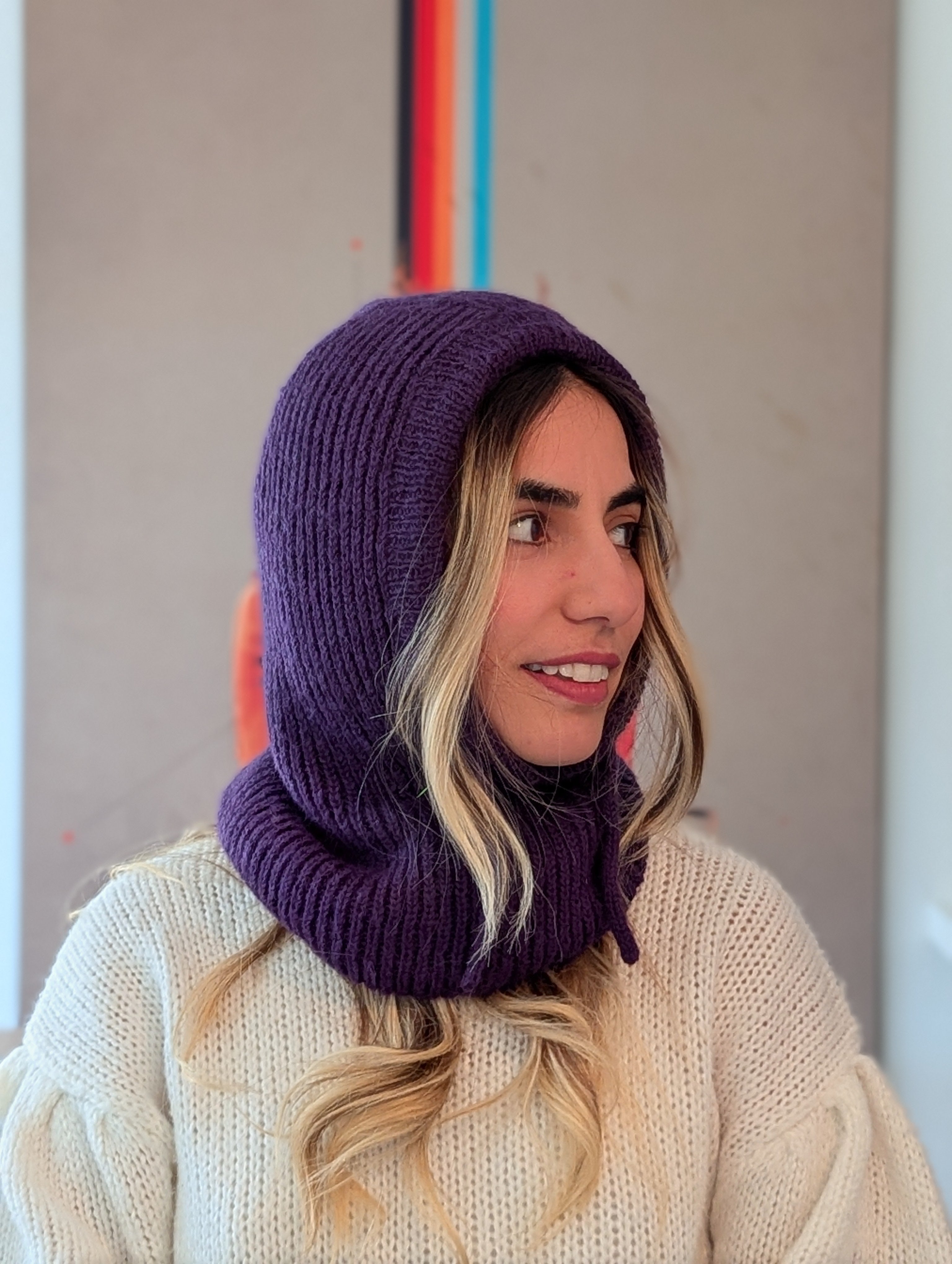 Woman wearing a purple knitted hood over a white sweater with a neutral background