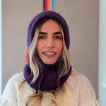 Person wearing a purple knitted cowl and white sweater against a neutral background