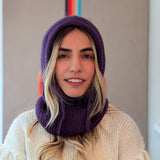 Person wearing a purple knitted cowl and white sweater against a neutral background