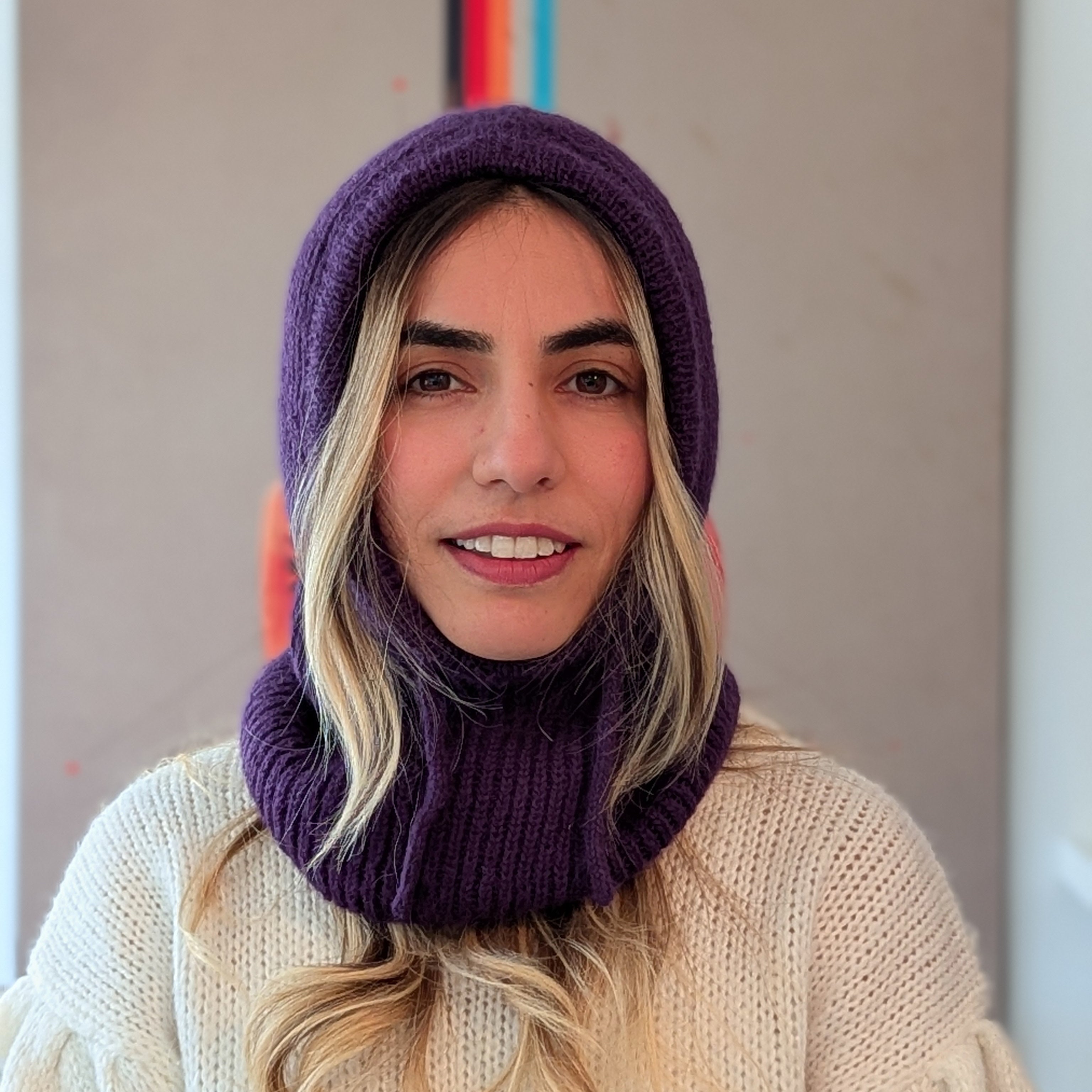 Person wearing a purple knitted cowl and white sweater against a neutral background
