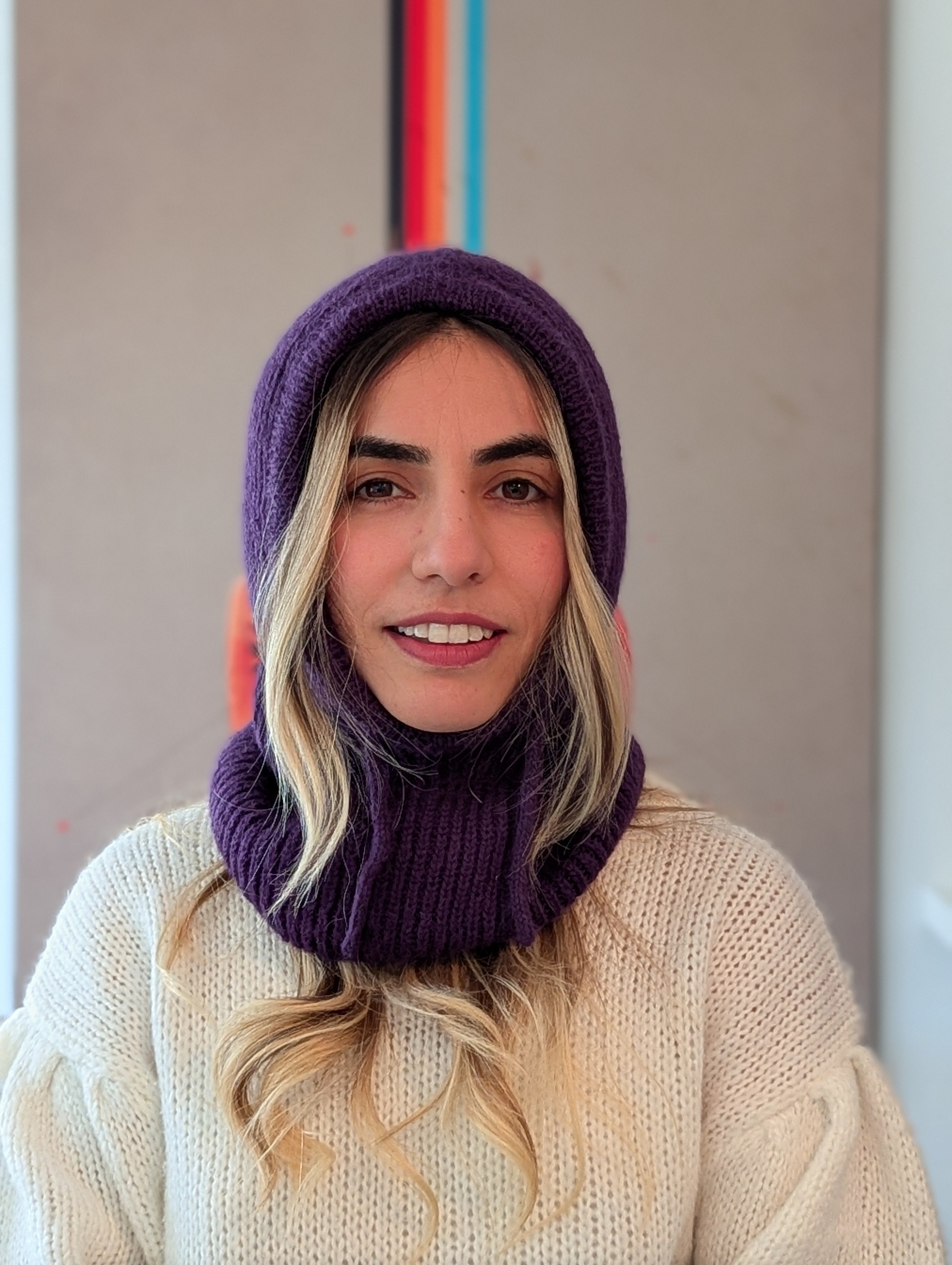 Person wearing a purple knitted cowl and white sweater against a neutral background