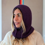 Woman wearing a purple knitted hood and beige sweater against a neutral background
