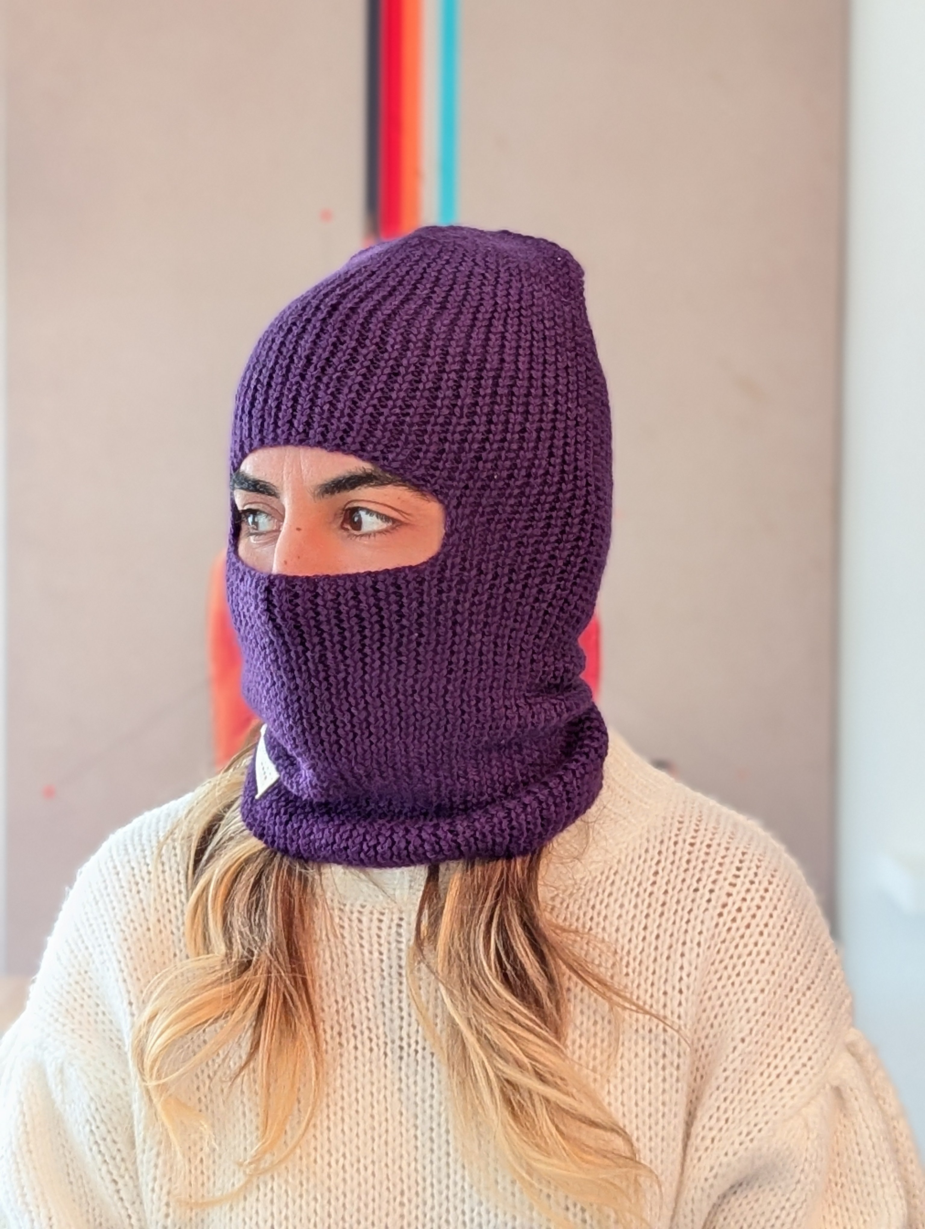 Person wearing a purple knitted balaclava against a neutral background