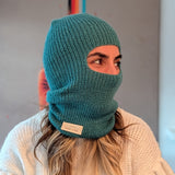 Person wearing a teal knitted balaclava with a visible brand label against a neutral background