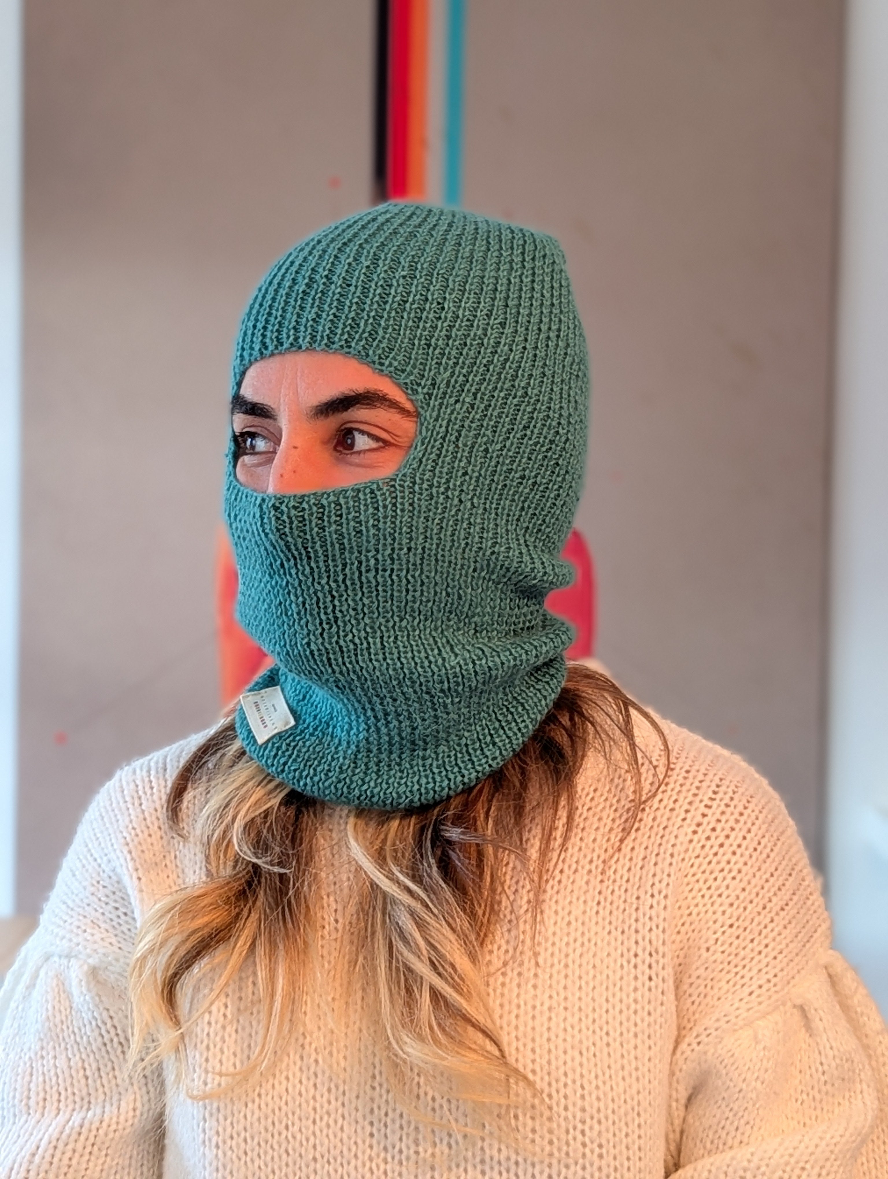 Person wearing a green knitted balaclava with a blurred background