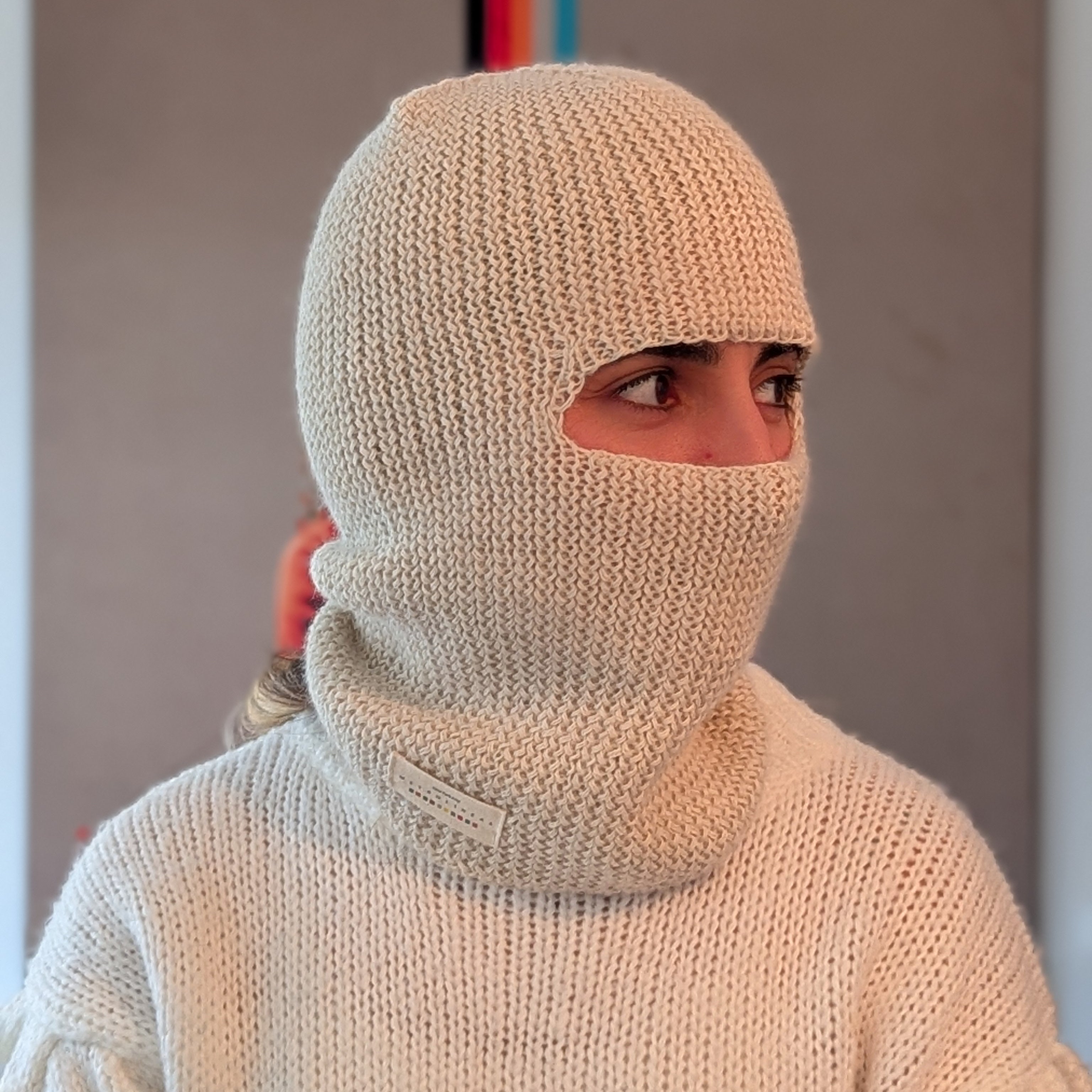 Person wearing a white knitted balaclava against a neutral background