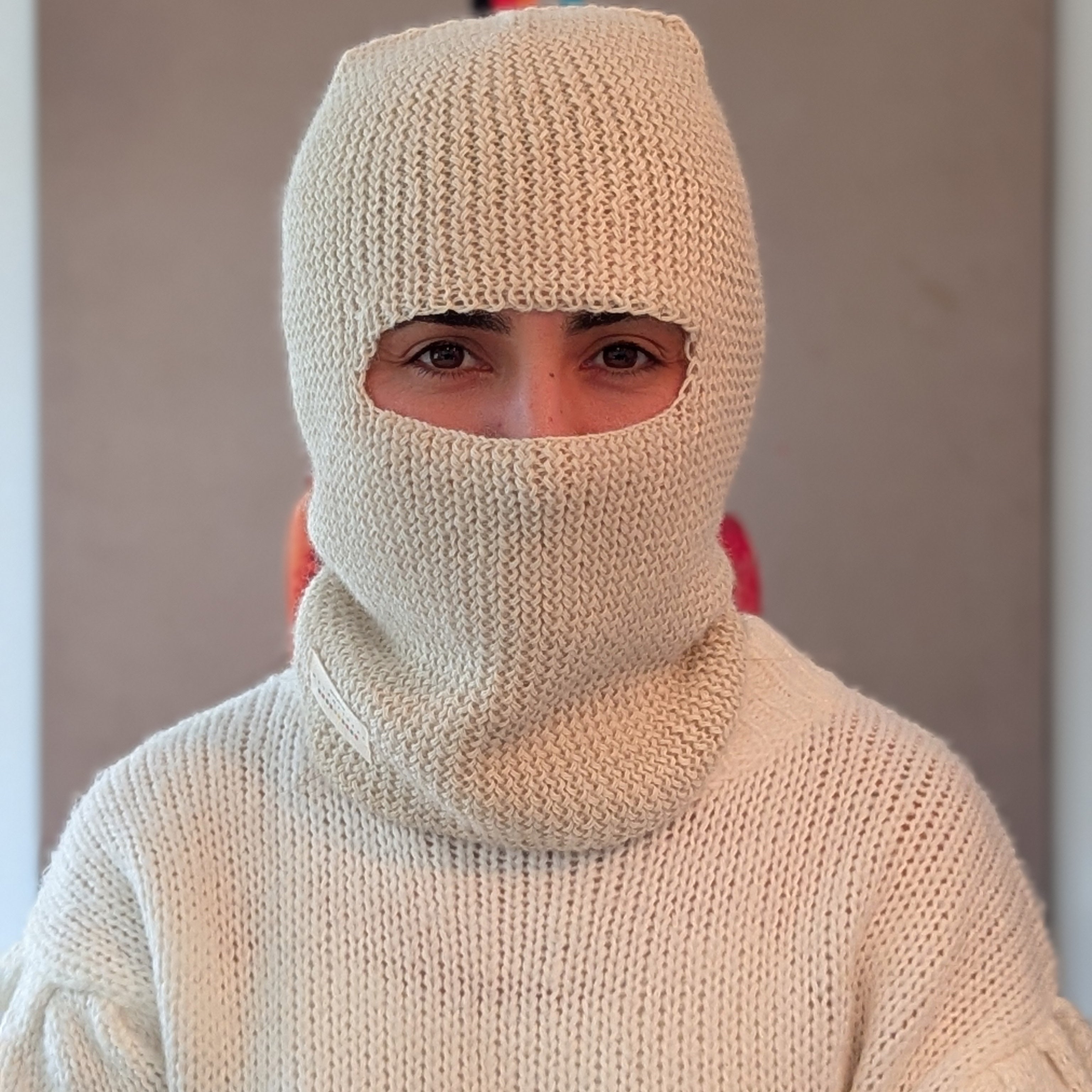 Person wearing a white knit balaclava and sweater against a plain background