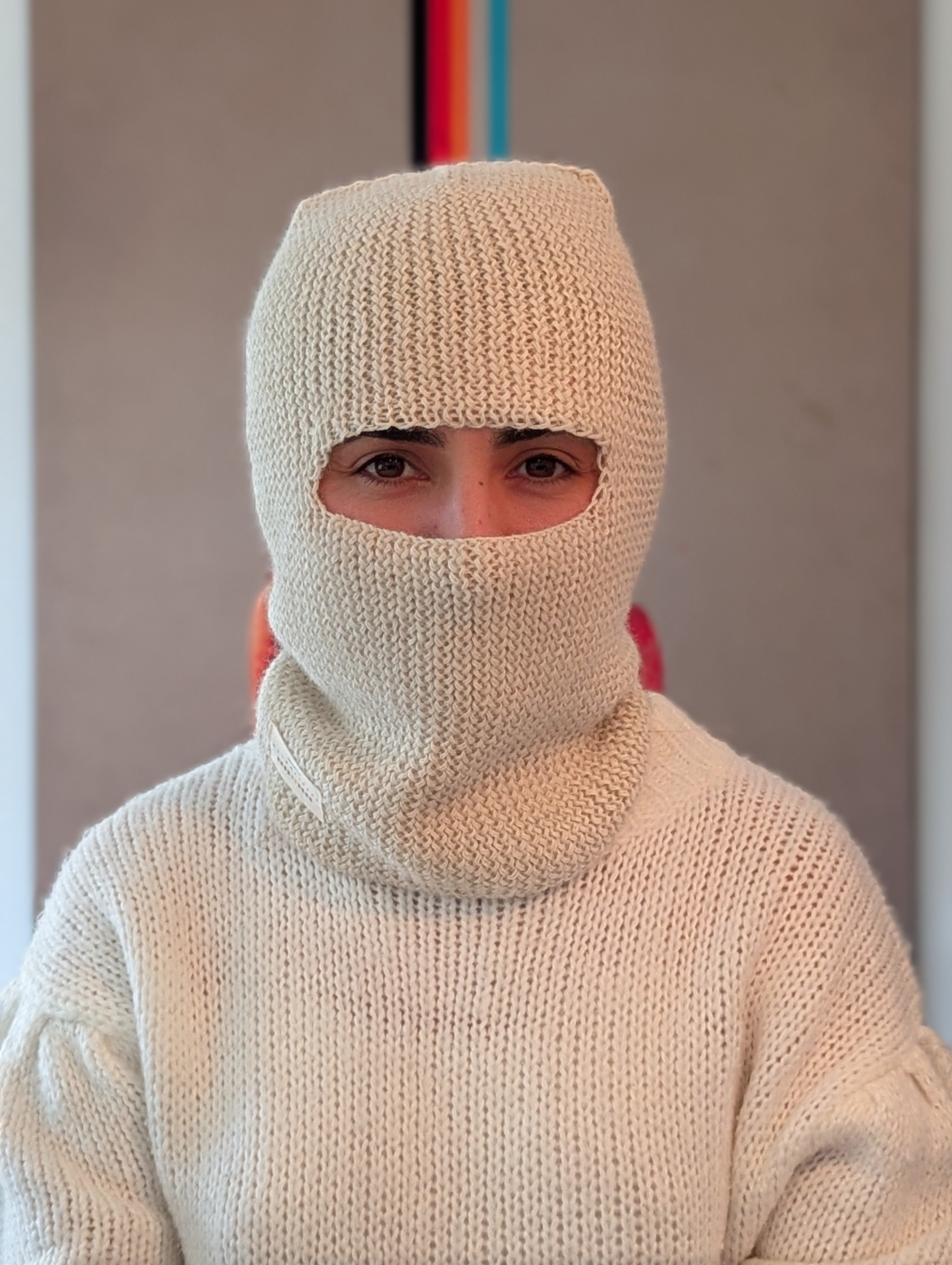 Person wearing a white knit balaclava and sweater against a plain background