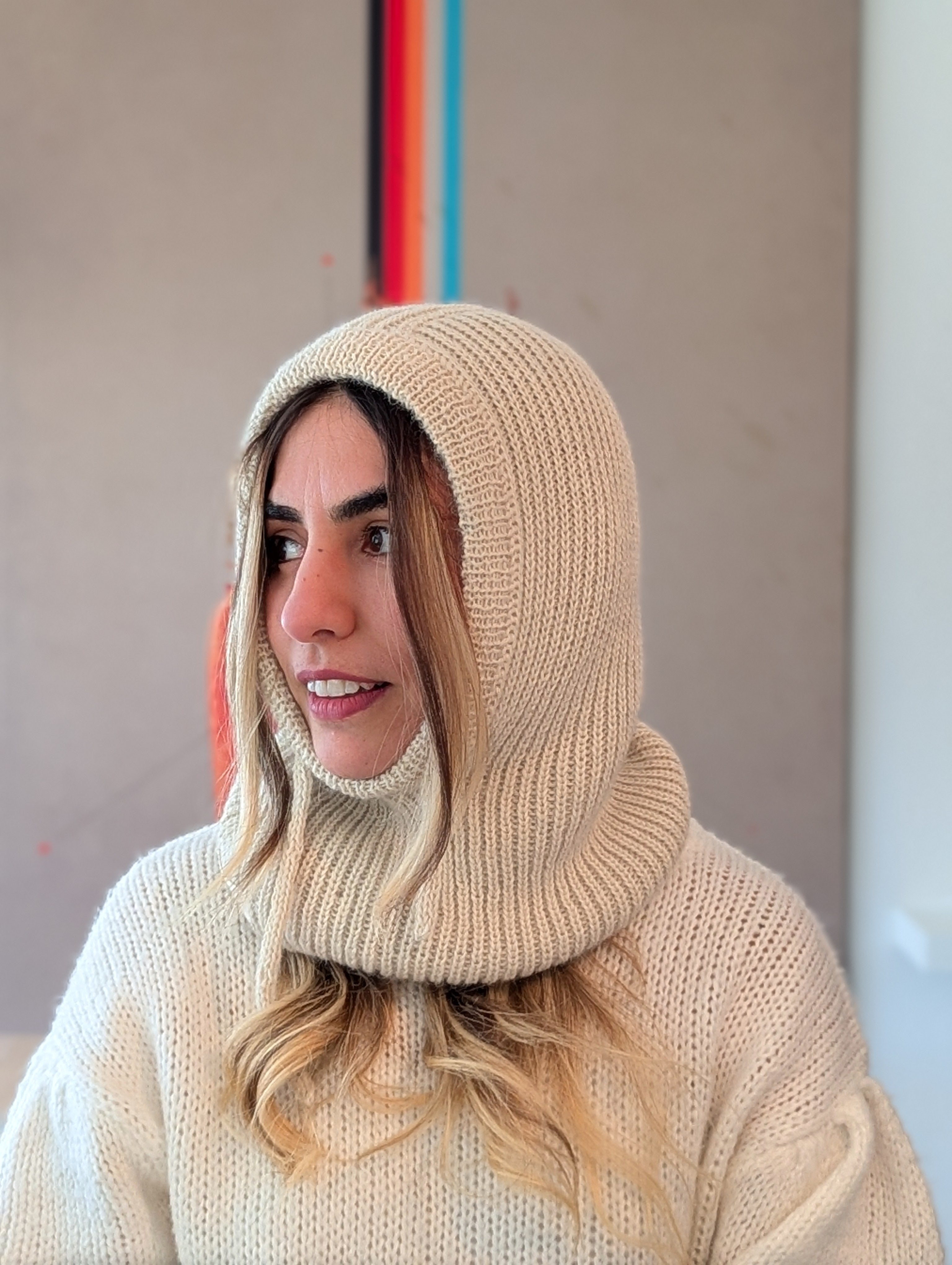 Person wearing a white knitted hood and sweater in an indoor setting