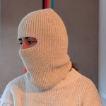 Person wearing a white knitted balaclava and sweater against a neutral background