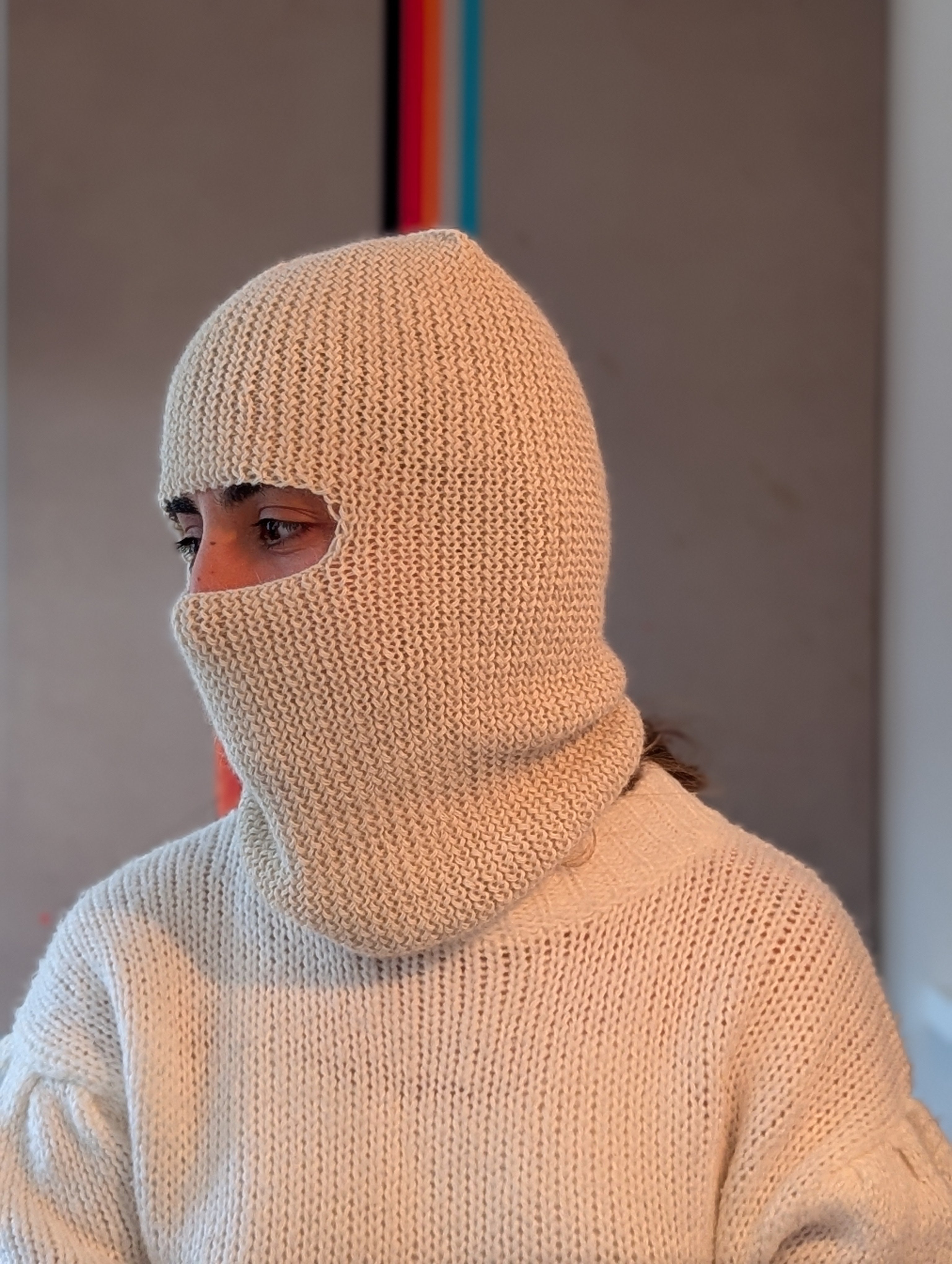 Person wearing a white knitted balaclava and sweater against a neutral background