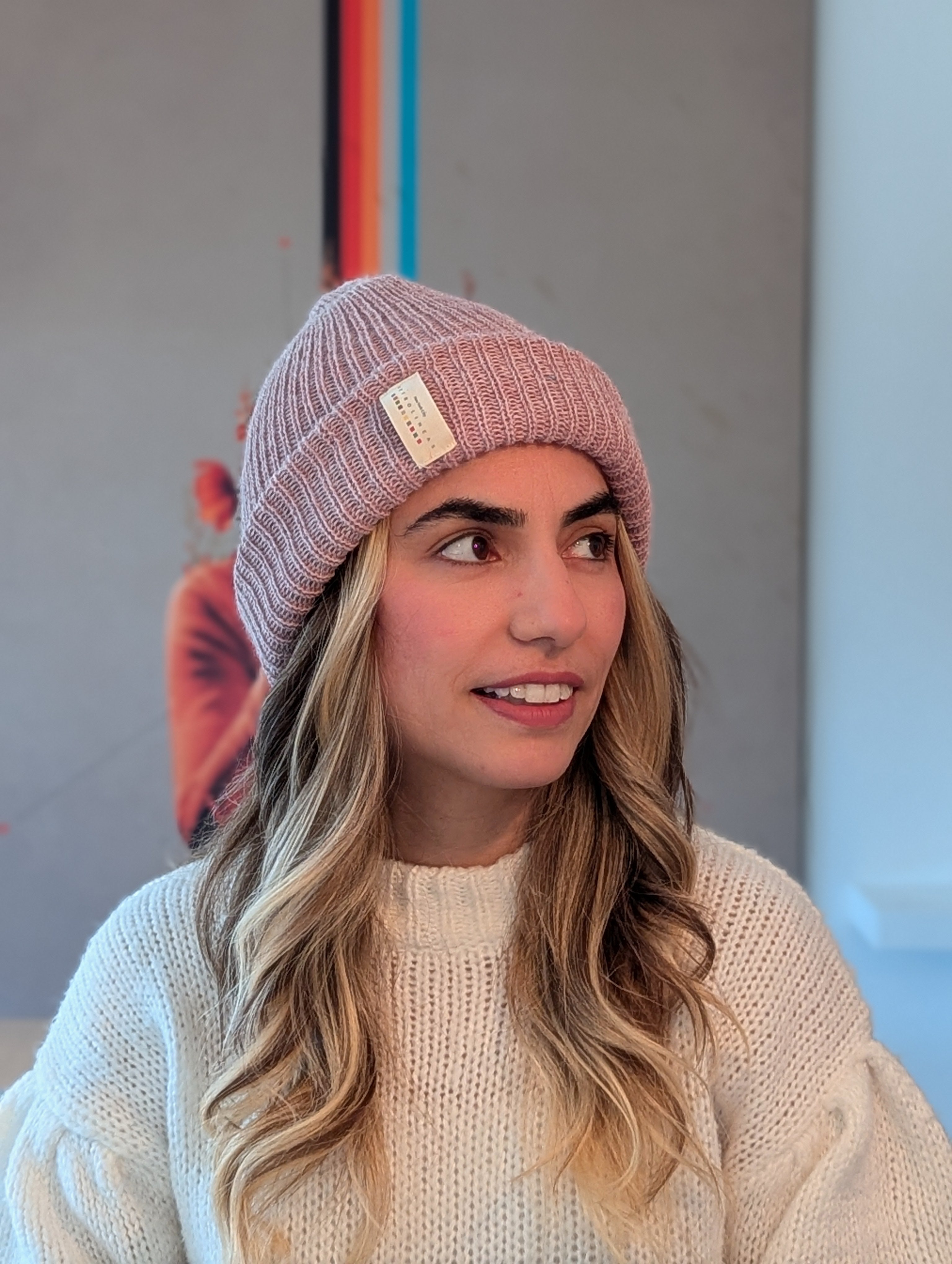 Woman wearing a pink beanie and light sweater against a neutral background