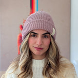 Woman wearing a pink knit beanie with a brand logo indoors.