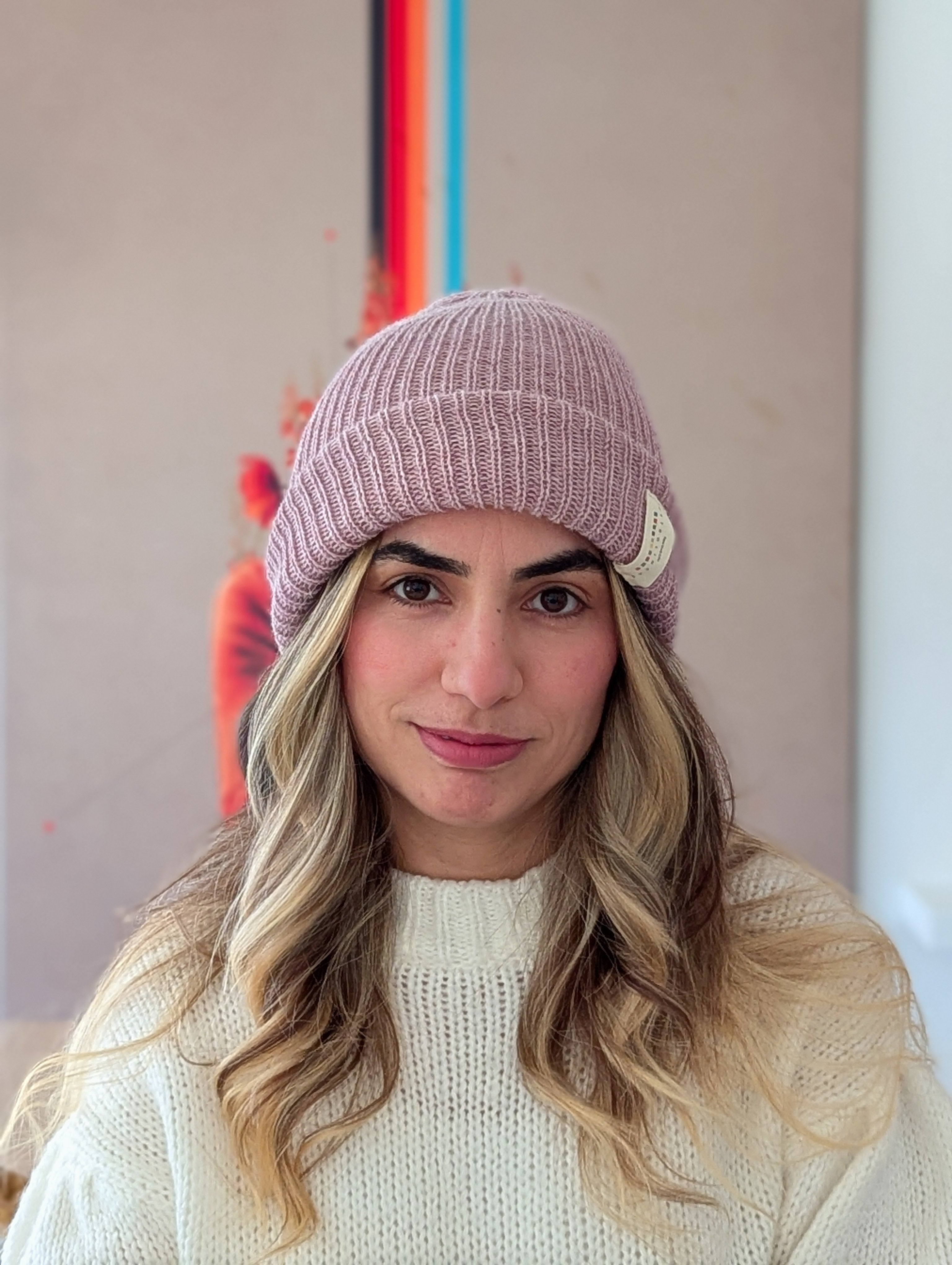 Woman wearing a pink knit beanie with a brand logo indoors.