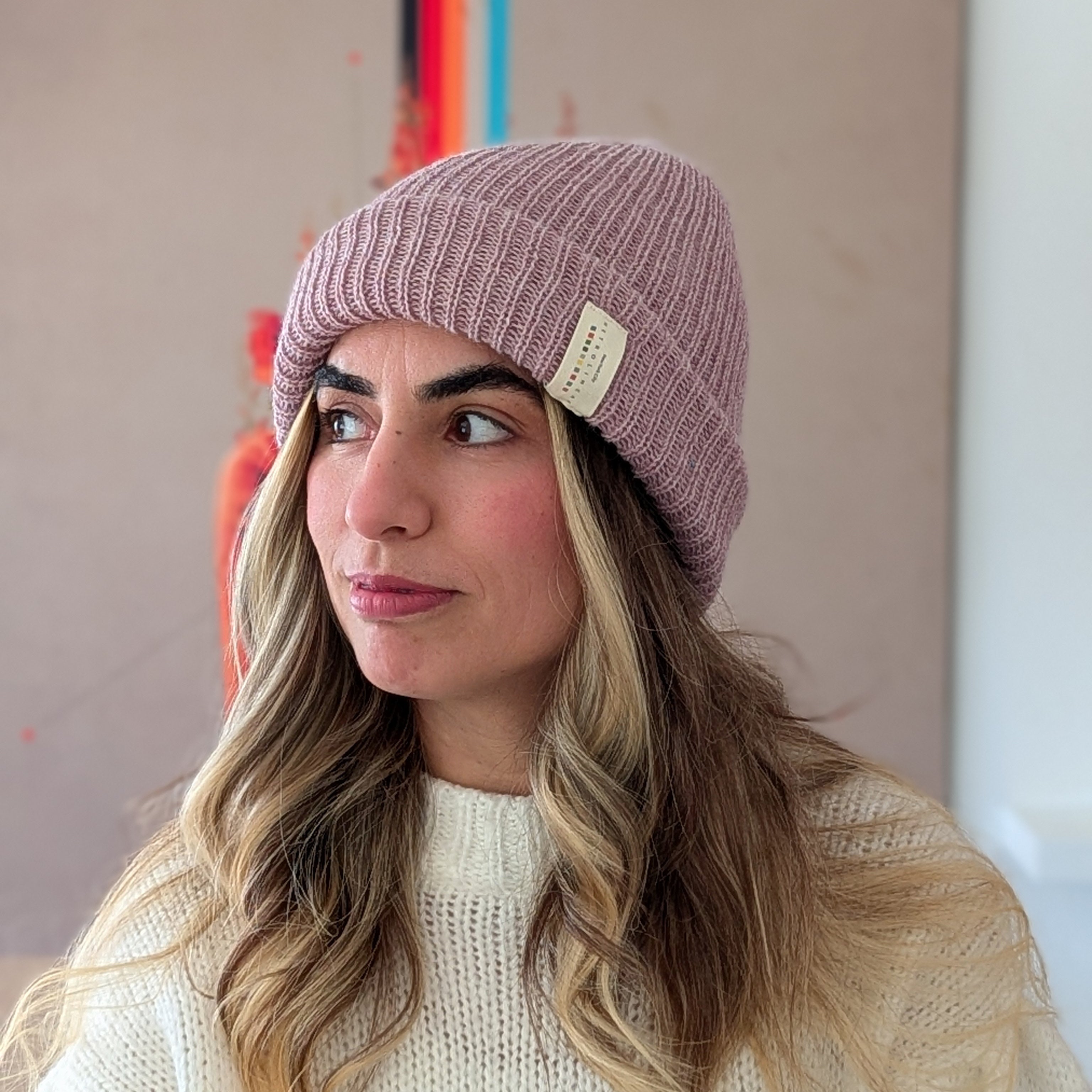Woman wearing a pink beanie with a brand logo against a neutral background