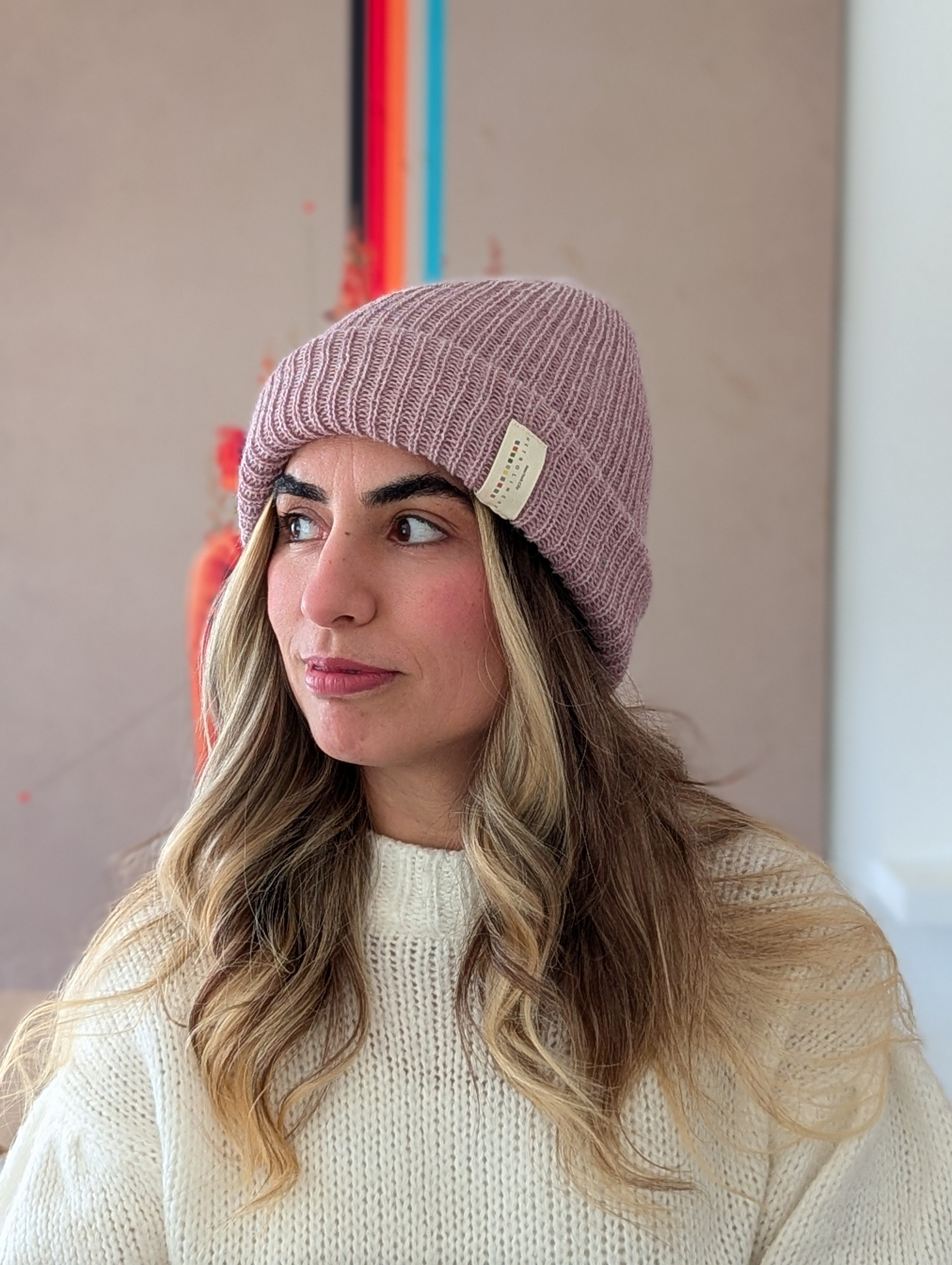 Woman wearing a pink beanie with a brand logo against a neutral background