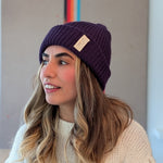 Woman wearing a purple beanie with a brand logo indoors