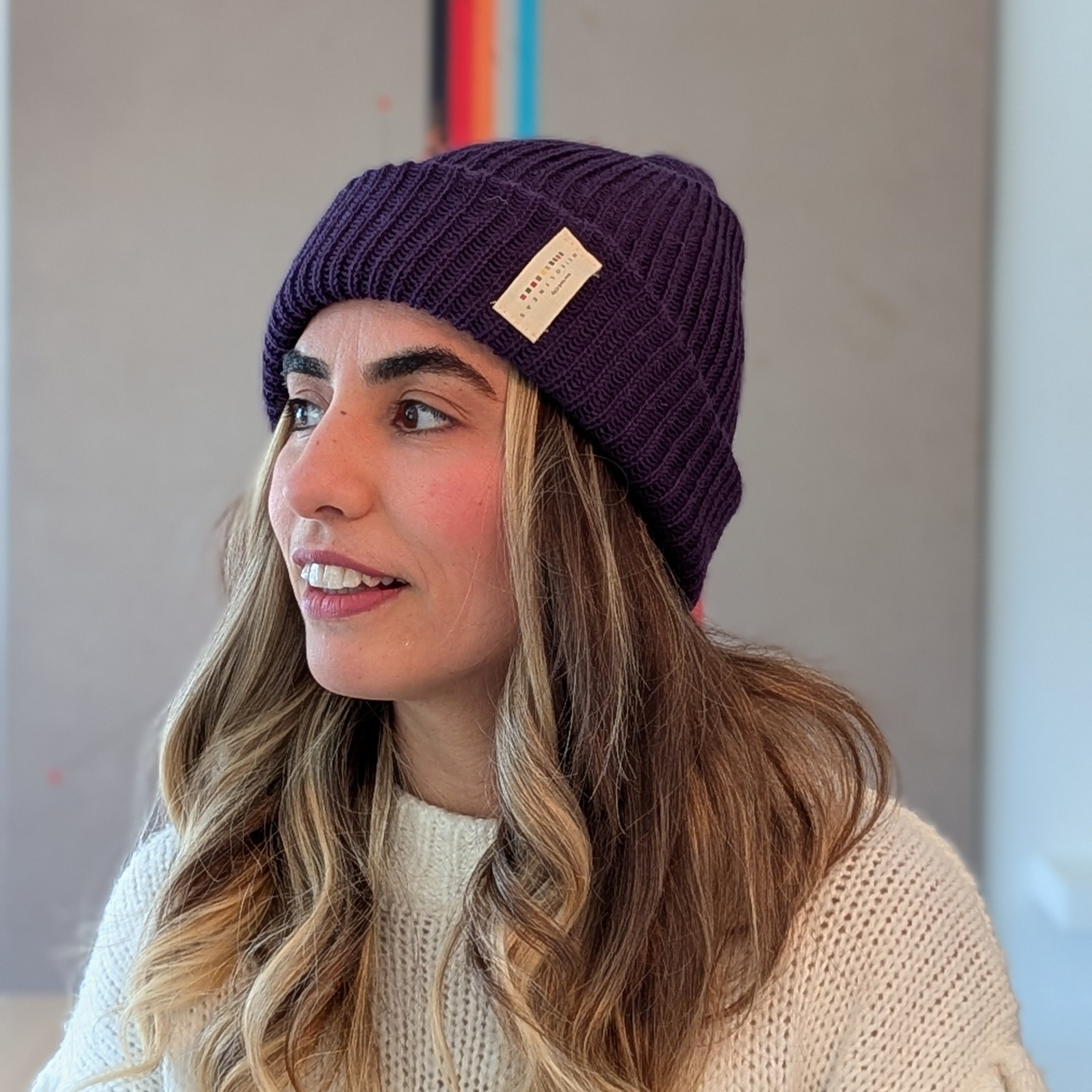 Woman wearing a purple beanie with a brand logo indoors