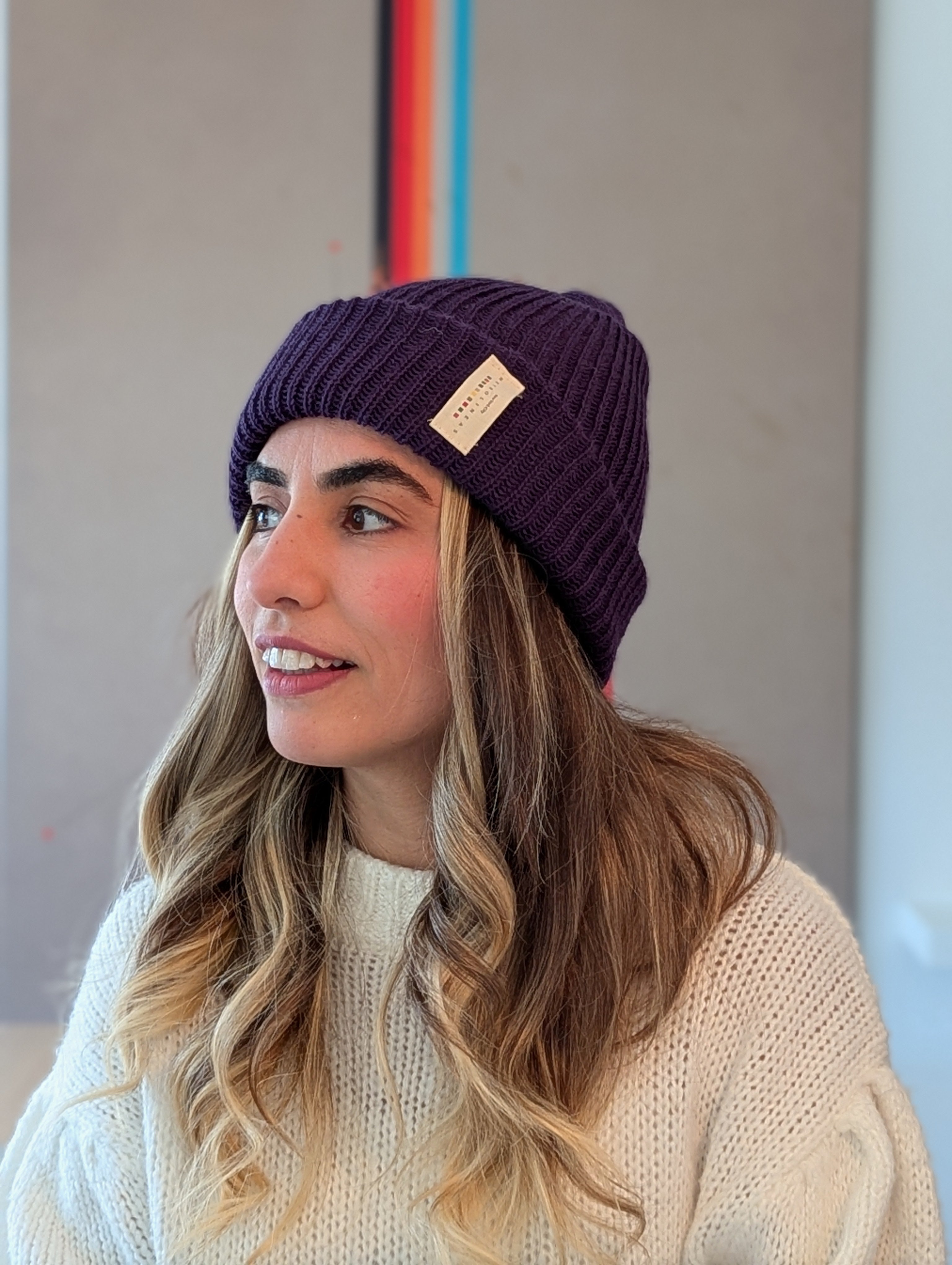 Woman wearing a purple beanie with a brand logo indoors