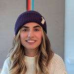 Woman wearing a purple beanie and white sweater with a colorful abstract painting in the background