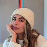 Woman wearing a white knit beanie and sweater indoors with a colorful abstract painting in the background.