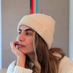 Woman wearing a white knit beanie and sweater, looking thoughtful.