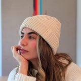 Woman wearing a white knit beanie and sweater, looking thoughtful.