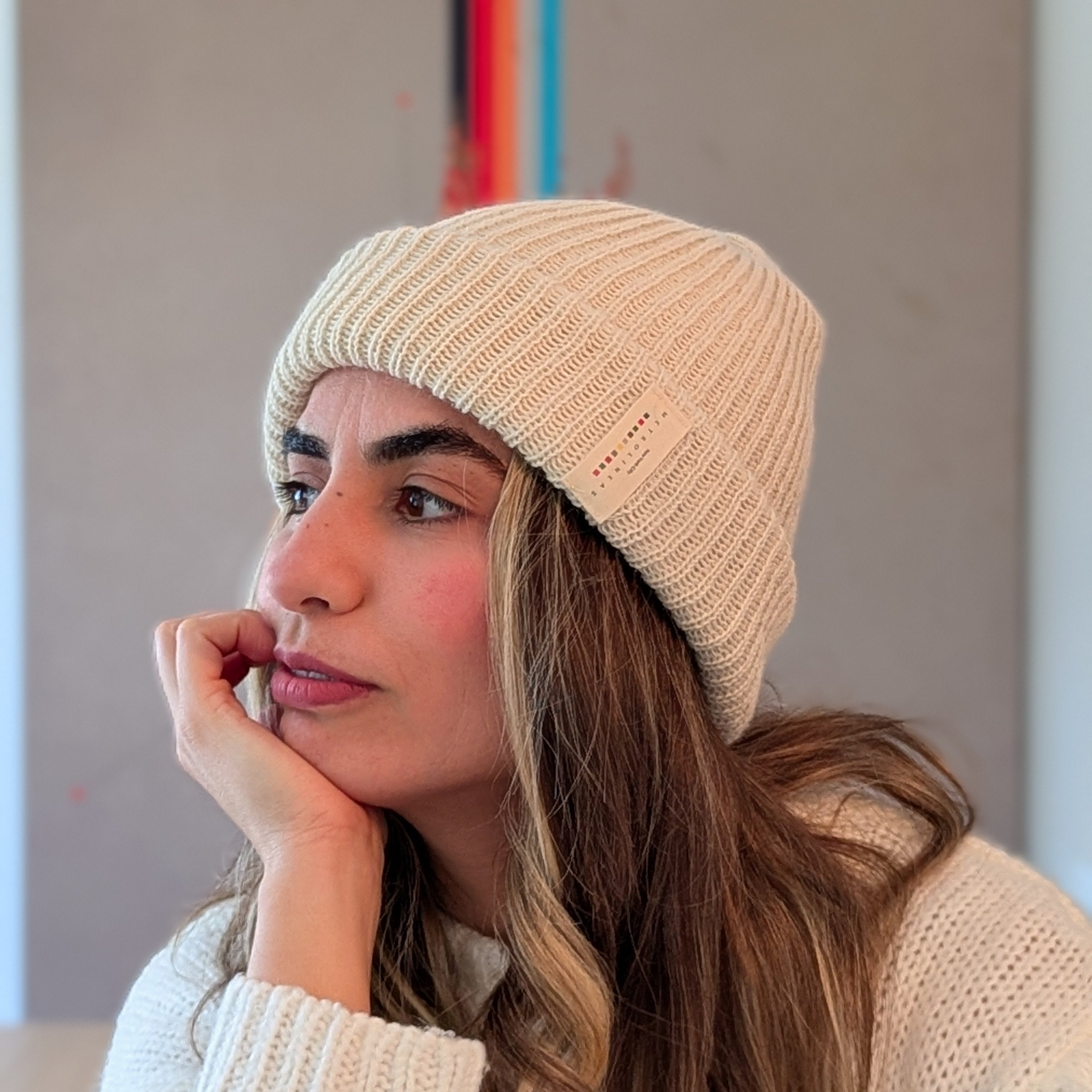 Woman wearing a white knit beanie and sweater, looking thoughtful.