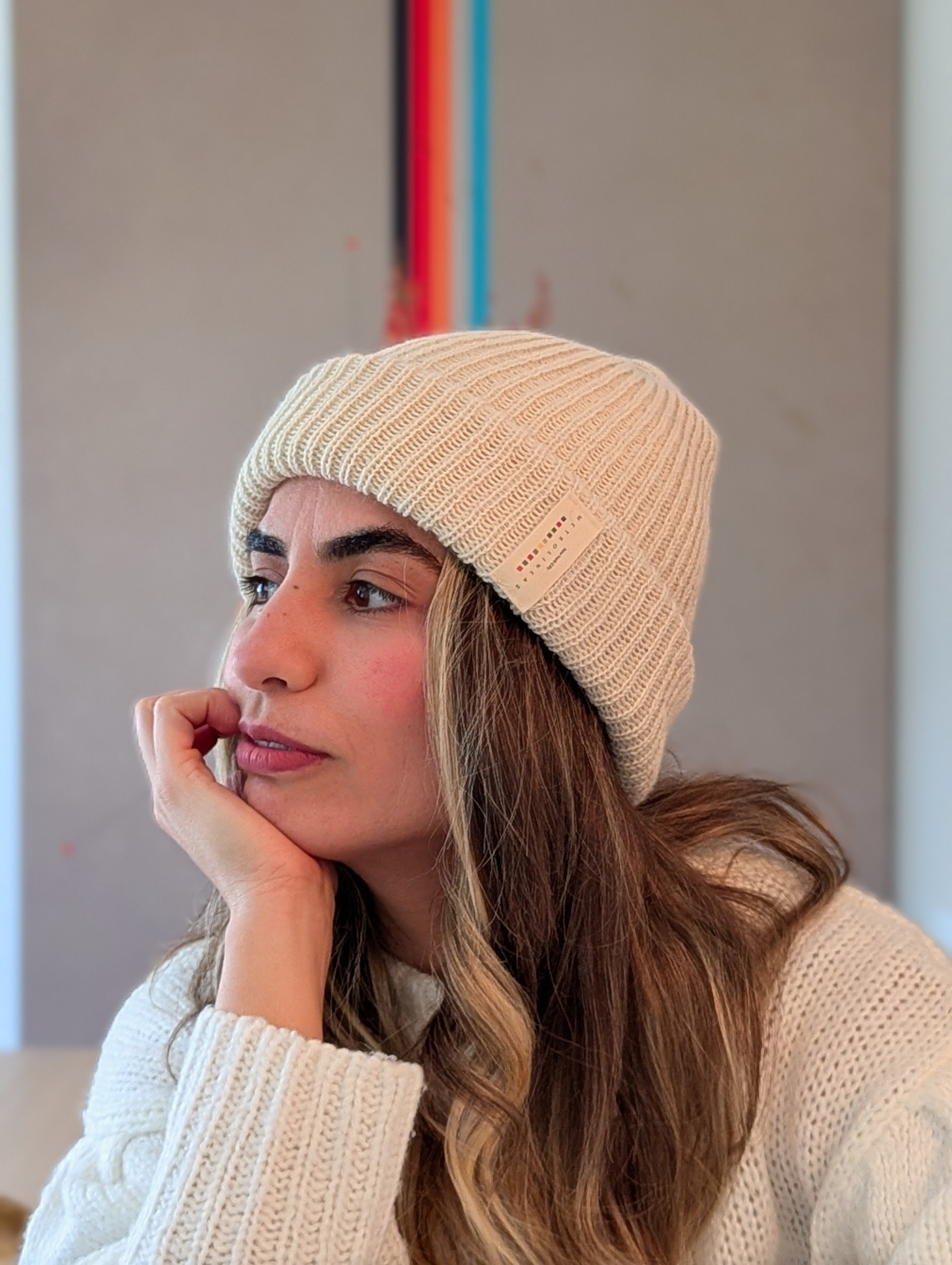 Woman wearing a white knit beanie and sweater, looking thoughtful.