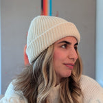 Woman wearing a white knit beanie and sweater against a neutral background