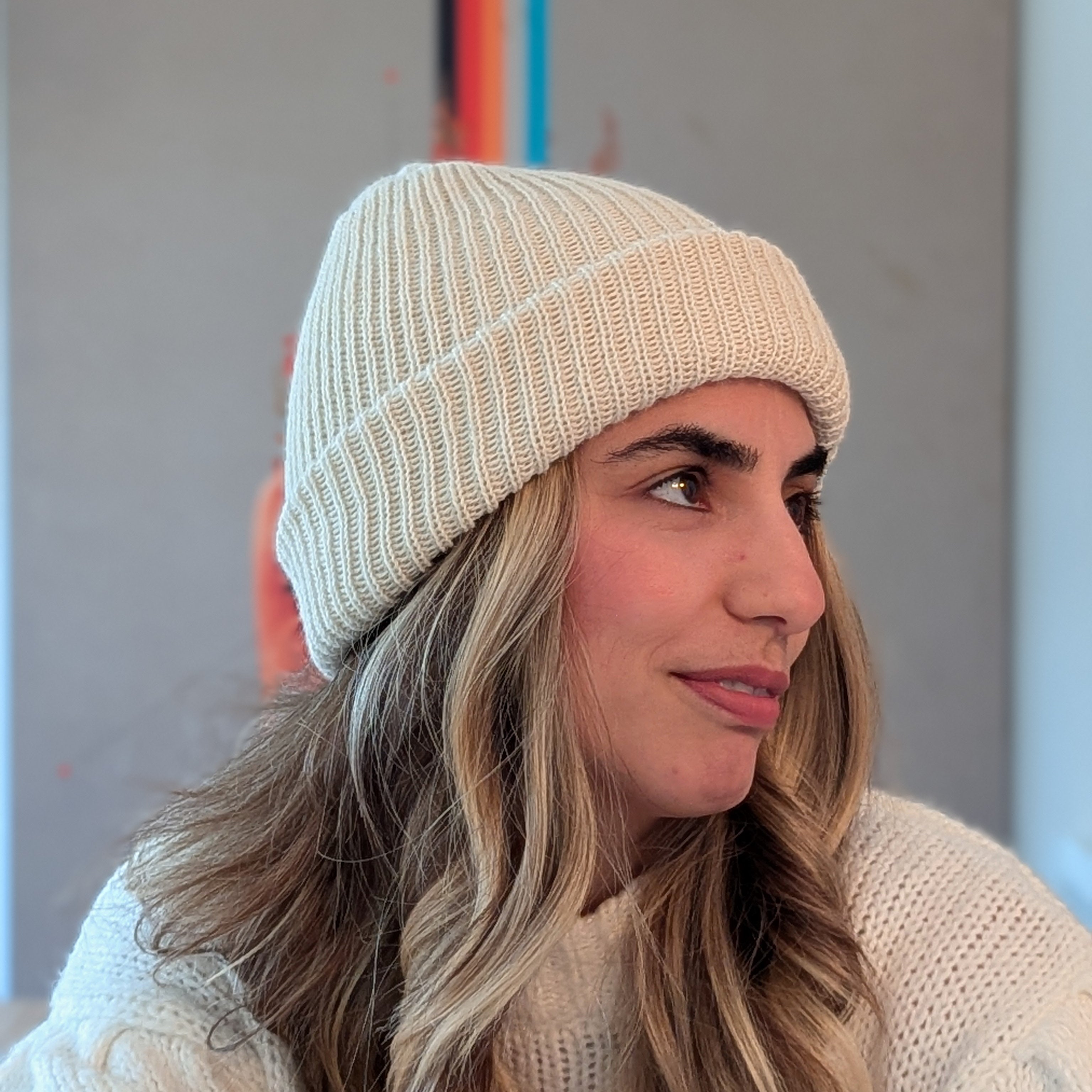 Woman wearing a white knit beanie and sweater against a neutral background