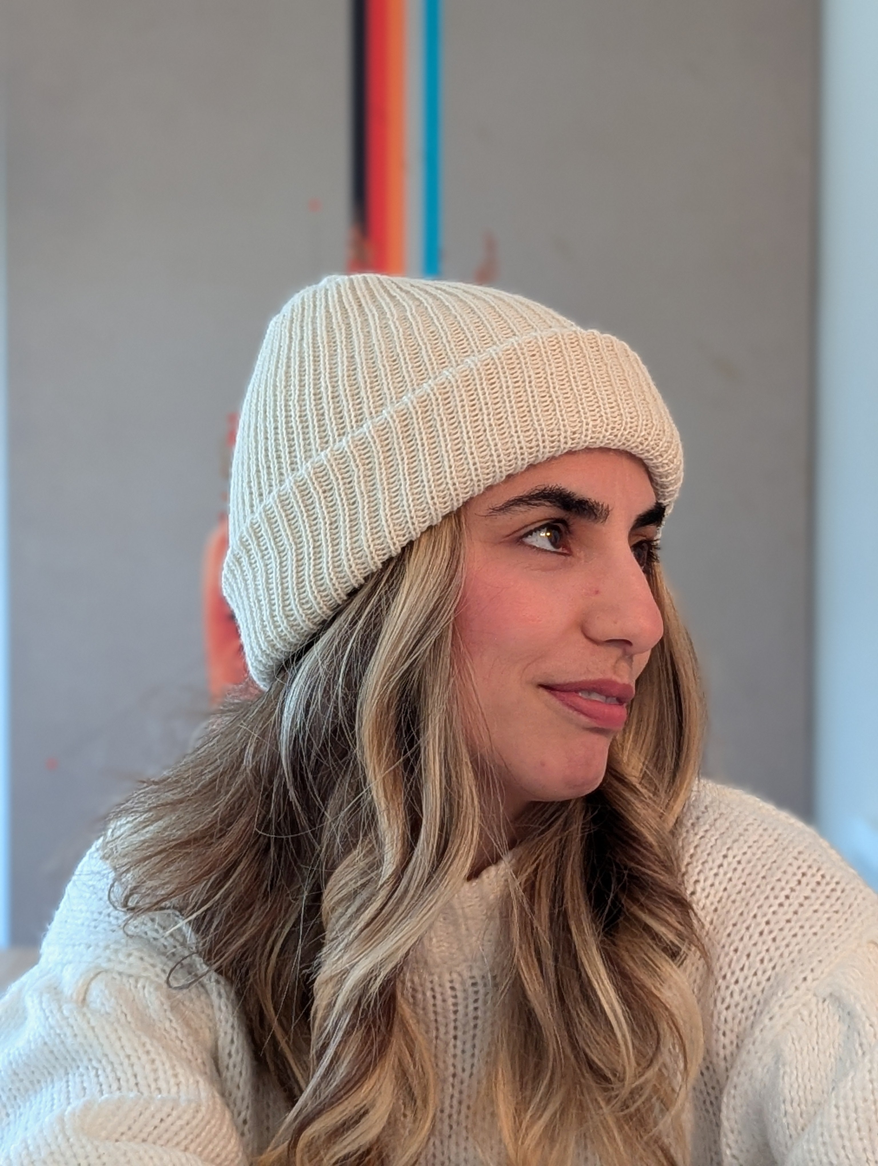 Woman wearing a white knit beanie and sweater against a neutral background