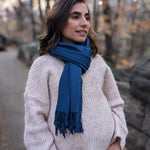 Woman wearing a blue scarf standing outdoors with trees in the background